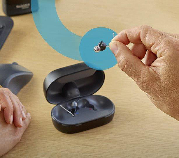 Otikon Hörgeräte Zeal in einer Hand und im Hintergrund die Ladebox