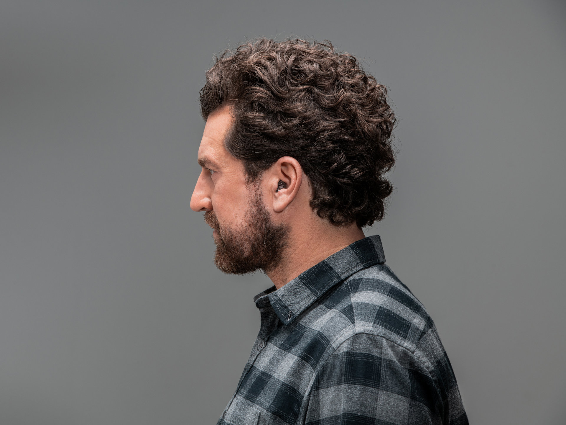 Mann mit lockigem Haar trägt ein Hörgerät im Ohr